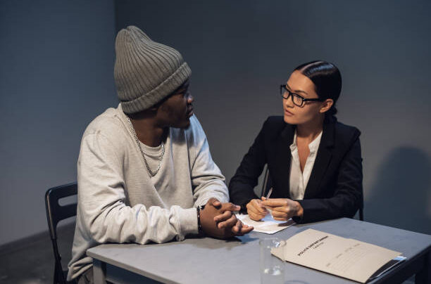 A pretty girl lawyer in glasses calms her client a black drug addict in the interrogation room.
